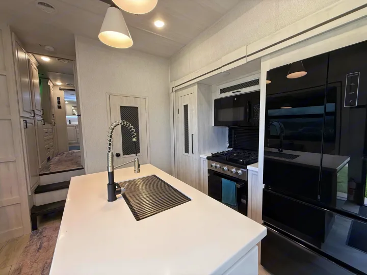 Explore this luxury RV rental's well-equipped kitchen. Features include a large island, stove, microwave, and modern black fridge.. East to West Ahara 2024