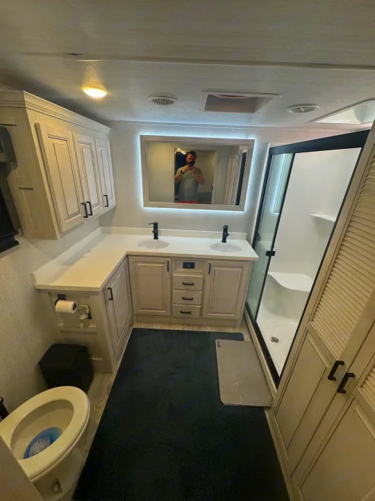 Full RV rental bathroom with dual sink vanity, modern black fixtures, backlit mirror, standing shower, and toilet.. East to West Ahara 2024