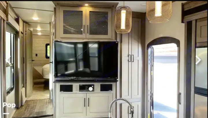 RV rental interior: modern living area with TV, cabinets, hallway, and an open side door. Bright and inviting.. Keystone RV Raptor Toy Hauler 2020