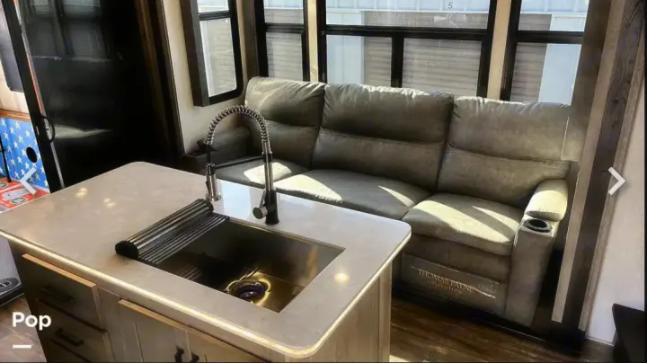 Modern RV rental: a bright living area with a sleek kitchen island, sink, and plush recliner sofa by windows.. Keystone RV Raptor Toy Hauler 2020