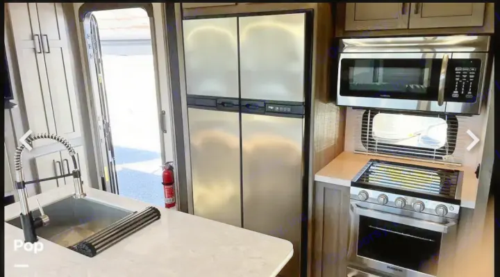 RV rental interior showing a full kitchen with stainless steel refrigerator, microwave, gas range, and large sink.. Keystone RV Raptor Toy Hauler 2020