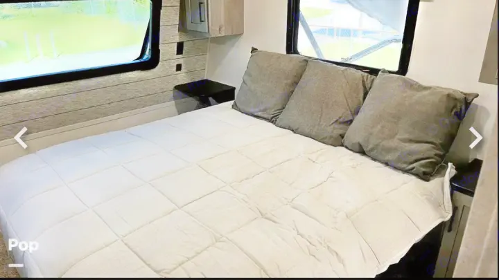 Explore comfort! This RV rental bedroom features a spacious bed, multiple dark pillows, and scenic windows for your travels.. Keystone RV Raptor Toy Hauler 2020