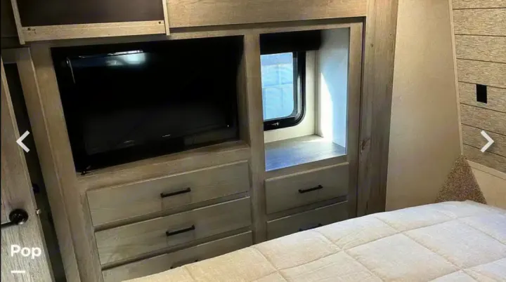Cozy RV rental bedroom with a mounted TV, built-in storage drawers, and a bright window next to the bed.. Keystone RV Raptor Toy Hauler 2020