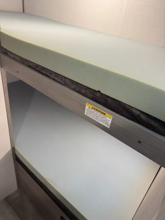 RV rental bunk bed with foam mattresses, showing a caution label on the frame for 300 lbs max load.. Dutchmen Coleman 17B 2024