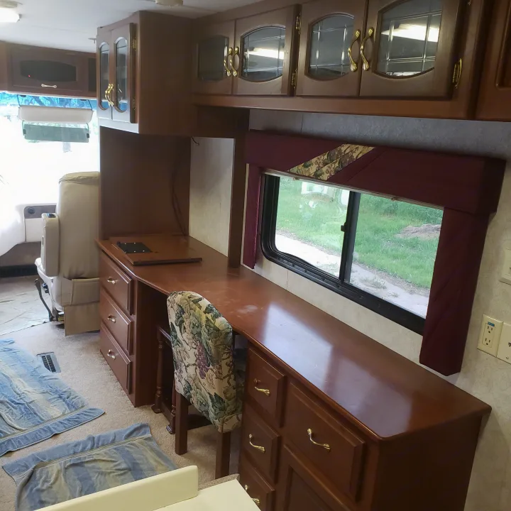 Explore this well-appointed RV rental interior featuring a large desk area, comfy chair, and overhead cabinets for storage.. Newmar Mountain Aire 1998