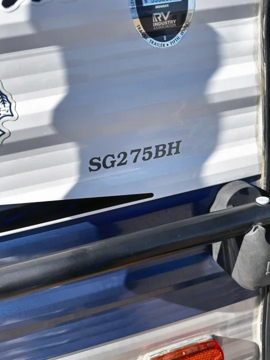 Close-up of an RV rental's white and blue exterior, featuring model SG275BH and an RV Industry Association sticker.. Keystone RV Springdale 2021
