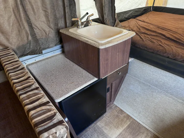 This RV rental interior features a compact kitchenette with a sink, Dometic fridge, and an adjacent sleeping area.. Palomino Other 2017