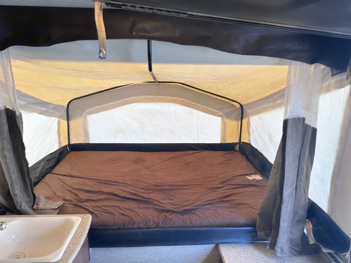 Inside an RV rental pop-up camper, showing the bed with brown blanket and a small sink area on the left.. Palomino Other 2017