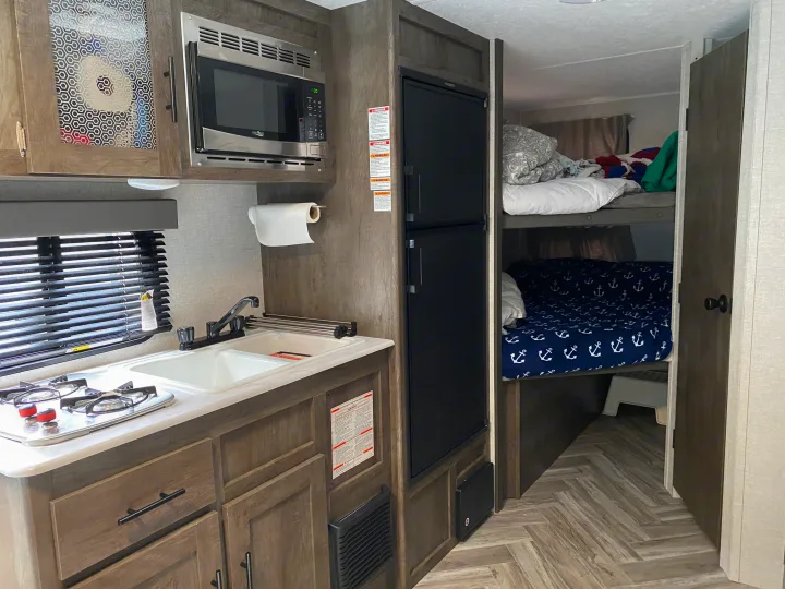 RV rental interior: compact kitchen with microwave, sink, stovetop, and bunk beds.. Forest River Wildwood Sport 2021
