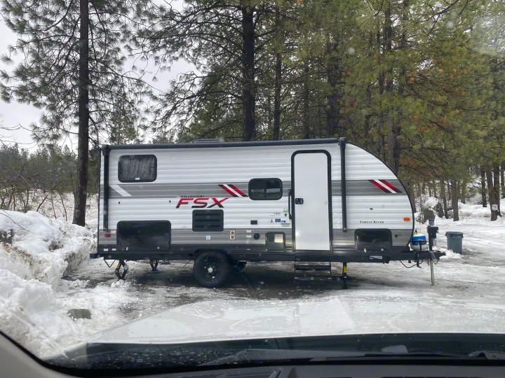 An RV rental, a Wildwood FSX travel trailer, sits in a snowy forest, ideal for winter camping.. Forest River Wildwood Sport 2021