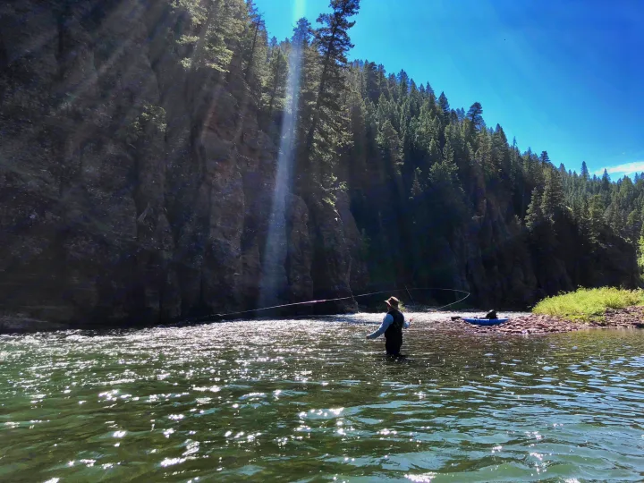 Scenic fly fishing on a sunlit river, flanked by cliffs & forests. Discover wild places with an RV rental.. Entegra Coach Qwest 2019