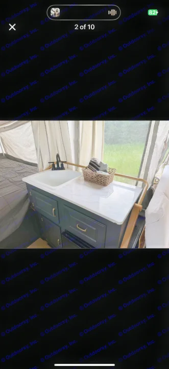 Inside an RV rental: a compact sink with black faucet, white marble counter, and dark cabinets. Cozy camping setup!. Coleman Grand Tour 2002