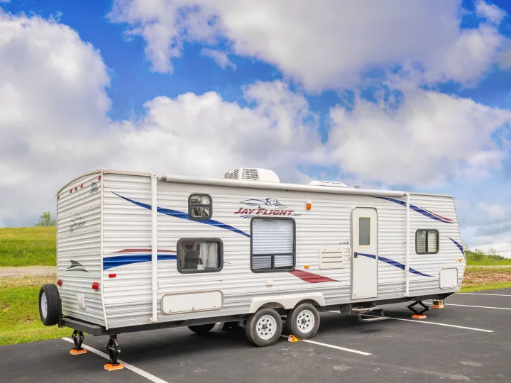 A white Jay Flight travel trailer rv rental is parked under a blue sky with white clouds, stabilizers extended, ready for adventure.. Jayco Jay Flight 2010