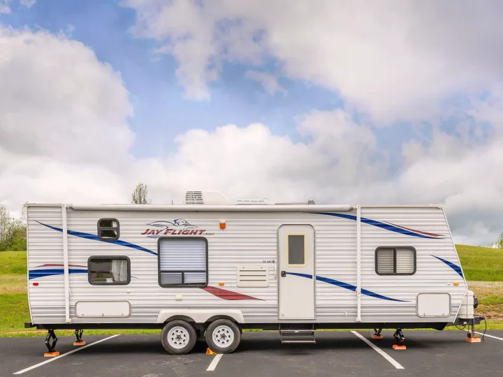 A white Jay Flight travel trailer RV rental, with blue and red graphics, parked on asphalt with leveling jacks, under a cloudy sky.. Jayco Jay Flight 2010