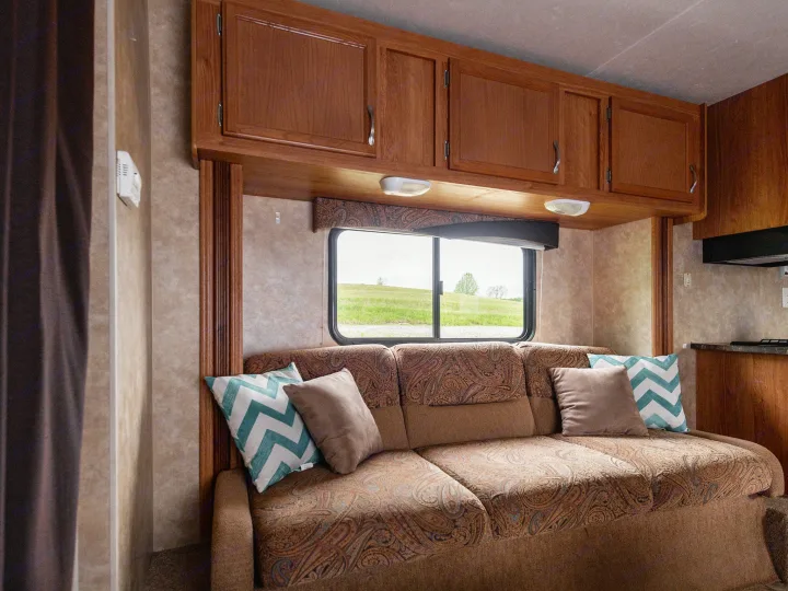 This cozy RV rental interior features a patterned sofa, wood cabinets, and a window offering a scenic outdoor view.. Jayco Jay Flight 2010