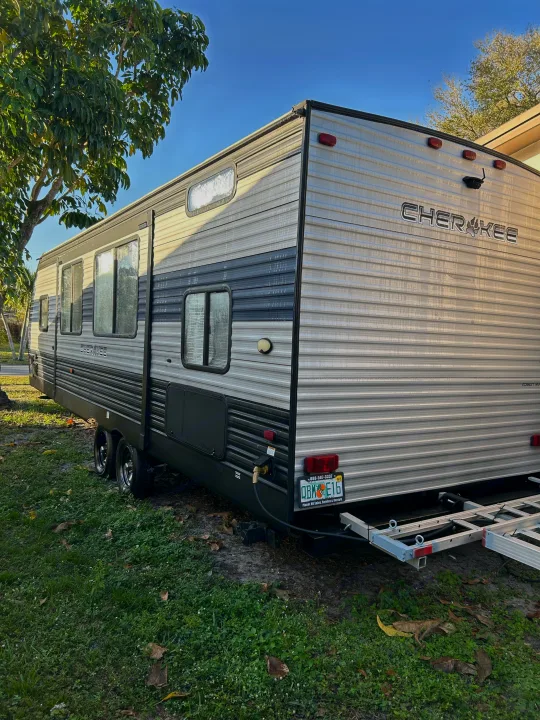 Silver and black Cherokee travel trailer RV parked on grass, ideal for rv rental adventures. Visible windows, wheels, and license plate.. Forest River Cherokee Grey Wolf 2020