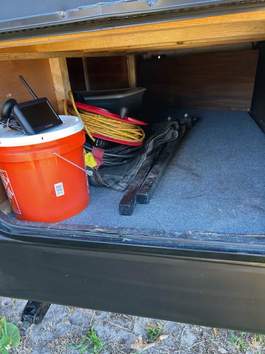 RV rental storage: An organized compartment holds a bucket, cables, and metal supports. A leveling jack is below.. Forest River Cherokee Grey Wolf 2020