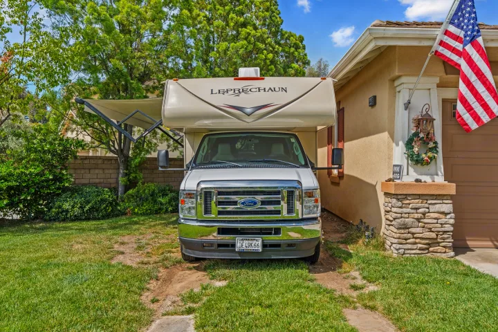 Front view of a white Ford Leprechaun RV rental parked in a grassy driveway with its side awning out.. COACHMEN Leprechaun 2023