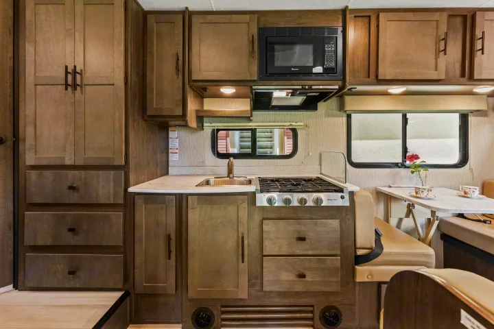 RV rental interior: A full kitchen and dining area with microwave, stove, sink, and cabinets for convenient travel.. COACHMEN Leprechaun 2023