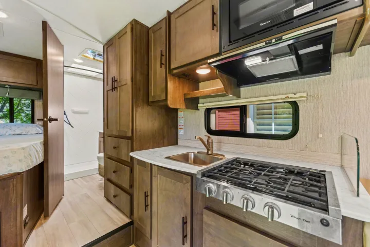 Modern RV rental interior: kitchen with stove/sink, peek into bedroom & bathroom. Ideal for your next camper trip.. COACHMEN Leprechaun 2023