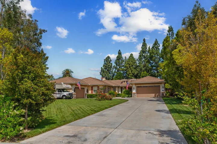 Tiled-roof home with a long driveway, green lawn, and an RV rental parked to the left.. COACHMEN Leprechaun 2023
