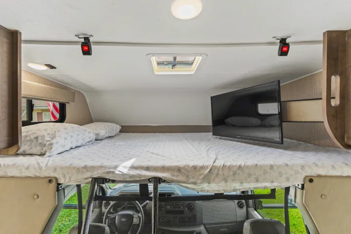 This RV rental's cab-over bunk offers a cozy sleeping area with a comfortable bed, TV, and skylight.. COACHMEN Leprechaun 2023