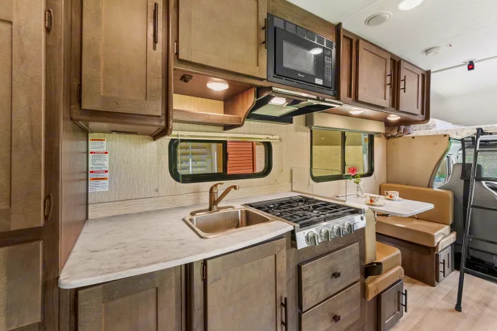 Explore this RV rental's well-appointed kitchen, featuring a sink, stove, and microwave, alongside a comfortable dining booth.. COACHMEN Leprechaun 2023