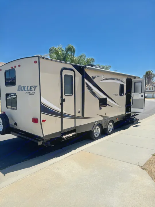 Tan Bullet Ultra Lite travel trailer (RV) with open door, on a sunny residential street, for rv rental.. Keystone RV Bullet Ultra Lite 2017