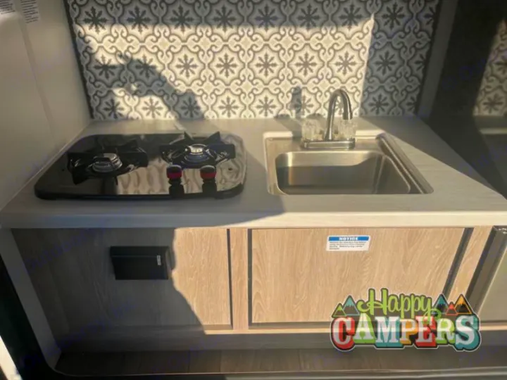 Compact RV rental kitchenette: two-burner stove, sink, and stylish backsplash. Perfect for your next adventure!. Riverside RV Intrepid 2023