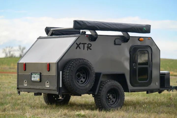 A rugged dark gray XTR off-road camper trailer in a grassy field. An ideal RV rental for backcountry adventures.. Venture XTR 2022