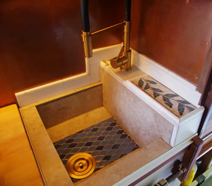 Custom RV rental sink featuring a brass faucet, elegant tile work, and a mosaic backsplash. Functional design for travel.. Dodge Ram Promaster 3500 2023
