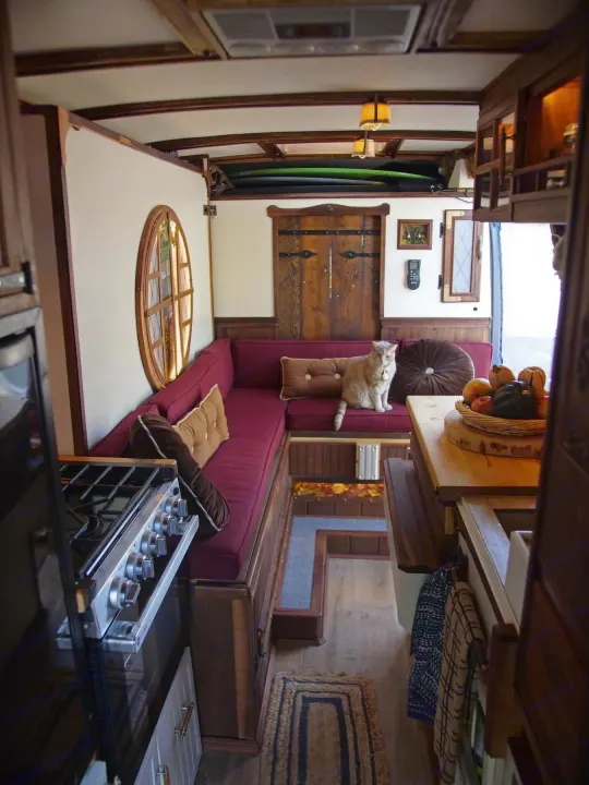 Cozy RV rental interior featuring custom wood, a kitchen area, and a cat relaxing on the burgundy sofa.. Dodge Ram Promaster 3500 2023
