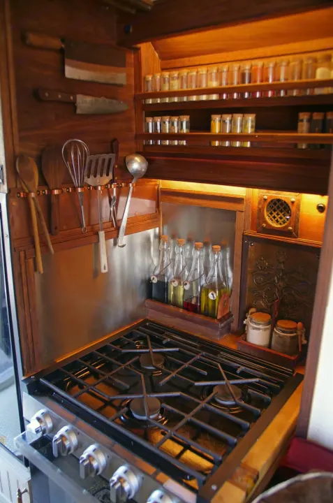 This RV rental features a cozy, fully stocked kitchen: gas stove, built-in spice racks, and hanging cooking tools.. Dodge Ram Promaster 3500 2023