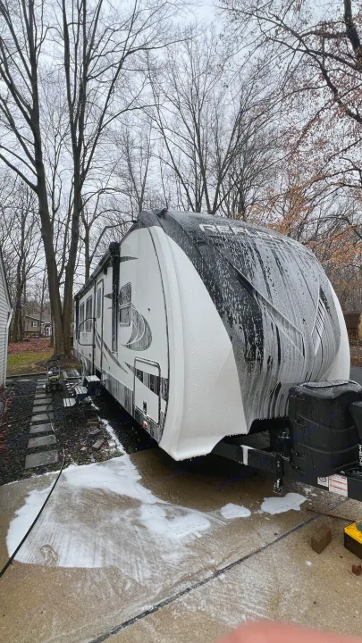 Large RV rental covered in white soap during a wash, parked in a residential driveway among bare trees.. Grand Design Reflection 2021