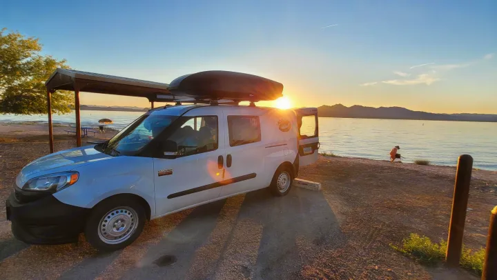 White Ram ProMaster City RV rental van at sunset by a lake, with mountains and a person near the water's edge.. Cascade Campers Ram Promaster City 2020