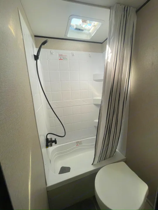 Clean RV rental bathroom with compact tub/shower, striped curtain, handheld shower, toilet, and skylight.. Starcraft Autumn Ridge 2023