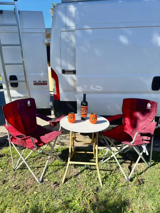 RV rental outdoor setup: White Ram ProMaster van with ladder, red chairs, table, & Bengals wine. Perfect for a stop.. Dodge Ram 1500 2020