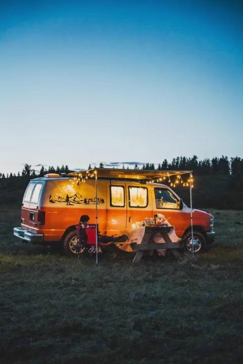 Experience van life with an RV rental: a cozy campervan lit by string lights, parked in a field for an evening picnic.. Ford Econoline E250supercab 2012