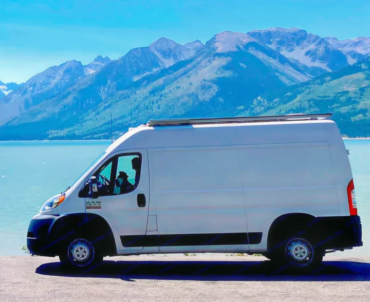 Scenic RV rental van parked by a serene lake with majestic mountains. Perfect for adventure travel!. Dodge Ram 1500 2020