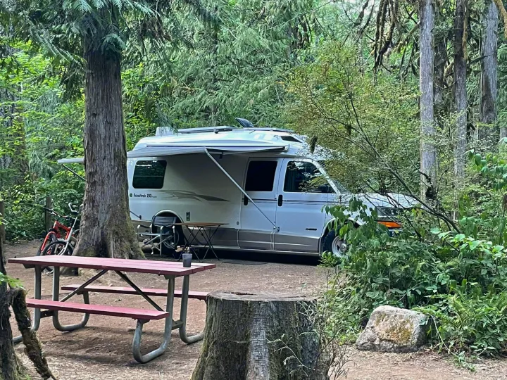 Relaxing RV rental setup: a Roadtrek camper van with awning extended at a green forest campsite with a picnic table.. Roadtrek 210 - Popular 2005