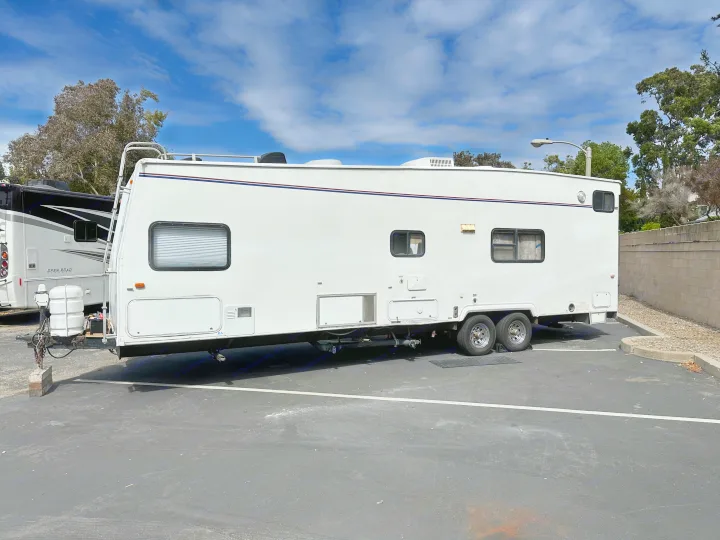 White travel trailer RV rental, with dual axles & propane, parked in a lot under blue skies.. Thor Motor Coach Tahoe 2003
