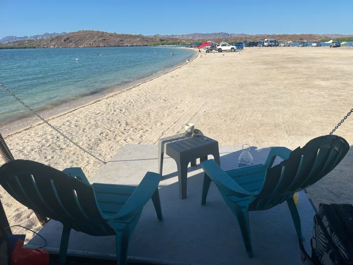 Relaxing beach view from an RV rental setup. Swimmers, seagulls, and vehicles line the sandy shore with mountains beyond.. Thor Motor Coach Tahoe 2003