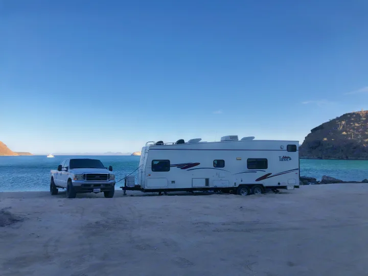 Scenic rv rental setup: A white truck and travel trailer parked on a sandy beach by turquoise water, with desert hills behind.. Thor Motor Coach Tahoe 2003