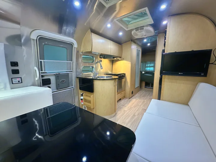 Modern Airstream RV rental interior: polished aluminum walls, light wood kitchen/cabinets, black table, and white seating.. Airstream Flying Cloud 2012