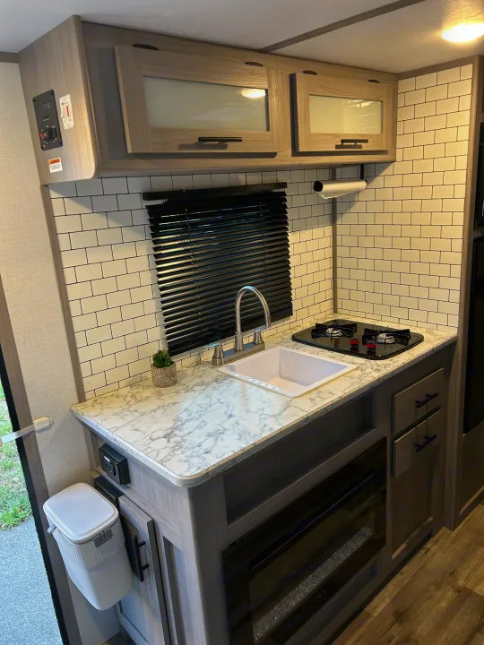 This RV rental's modern galley kitchen boasts white subway tiles, light wood cabinets, sink, and cooktop.. Coleman Coleman Lantern 17B 2023