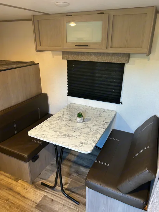 This RV rental features a bright dinette area with a faux marble table, dark brown seating, and overhead cabinets.. Coleman Coleman Lantern 17B 2023