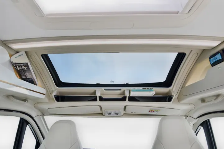 Bright RV rental interior: a wide overhead skylight and smart storage for magazines/books above modern front seats.. ELNAGH DUO XL 2025
