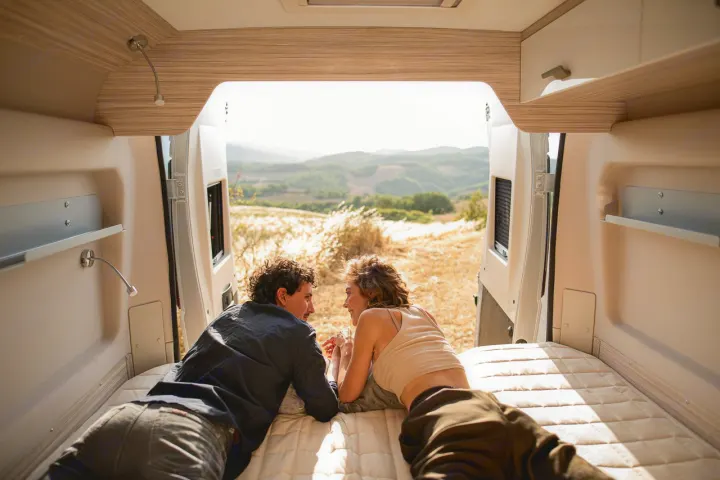 Relaxing couple in an RV rental, enjoying the scenic view from their bed. Perfect for a nature getaway.. ELNAGH DUO XL 2025