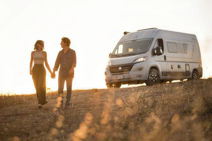 Romantic RV rental adventure: couple holding hands with their camper van in golden light.. ELNAGH DUO XL 2025