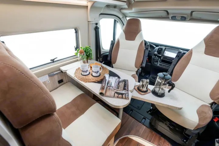 RV rental interior: A bright, modern camper van living space with a table set for coffee, cozy seating, and the driver's cab.. ELNAGH DUO XL 2025